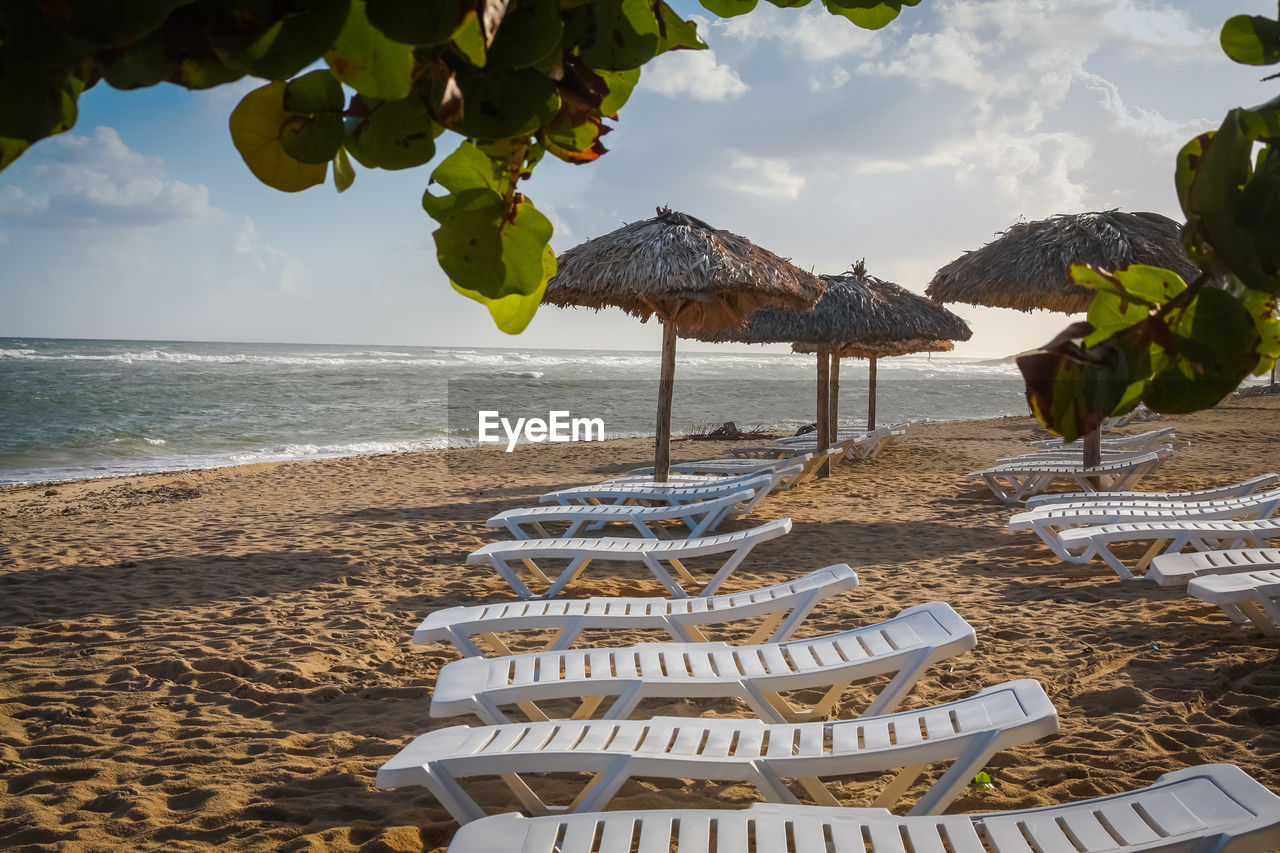 Empty deck chairs and parasols at beach against sky