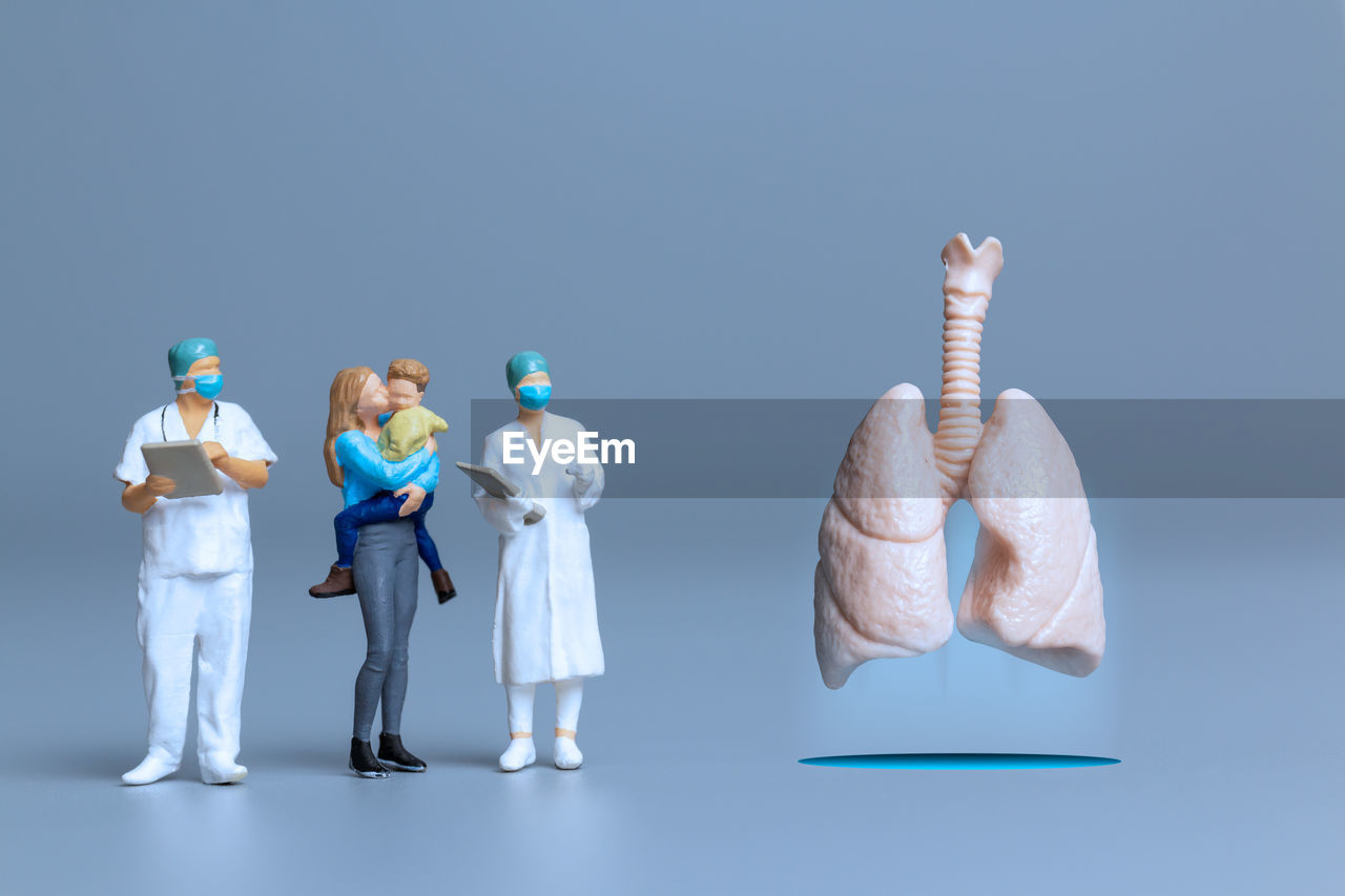 studio shot, full length, indoors, colored background, occupation, adult, blue, science, figurine, cooperation, blue background, healthcare and medicine, men, business, women, female, copy space, teamwork, group of people, standing, coworker, toy, cartoon, protection, clothing, person