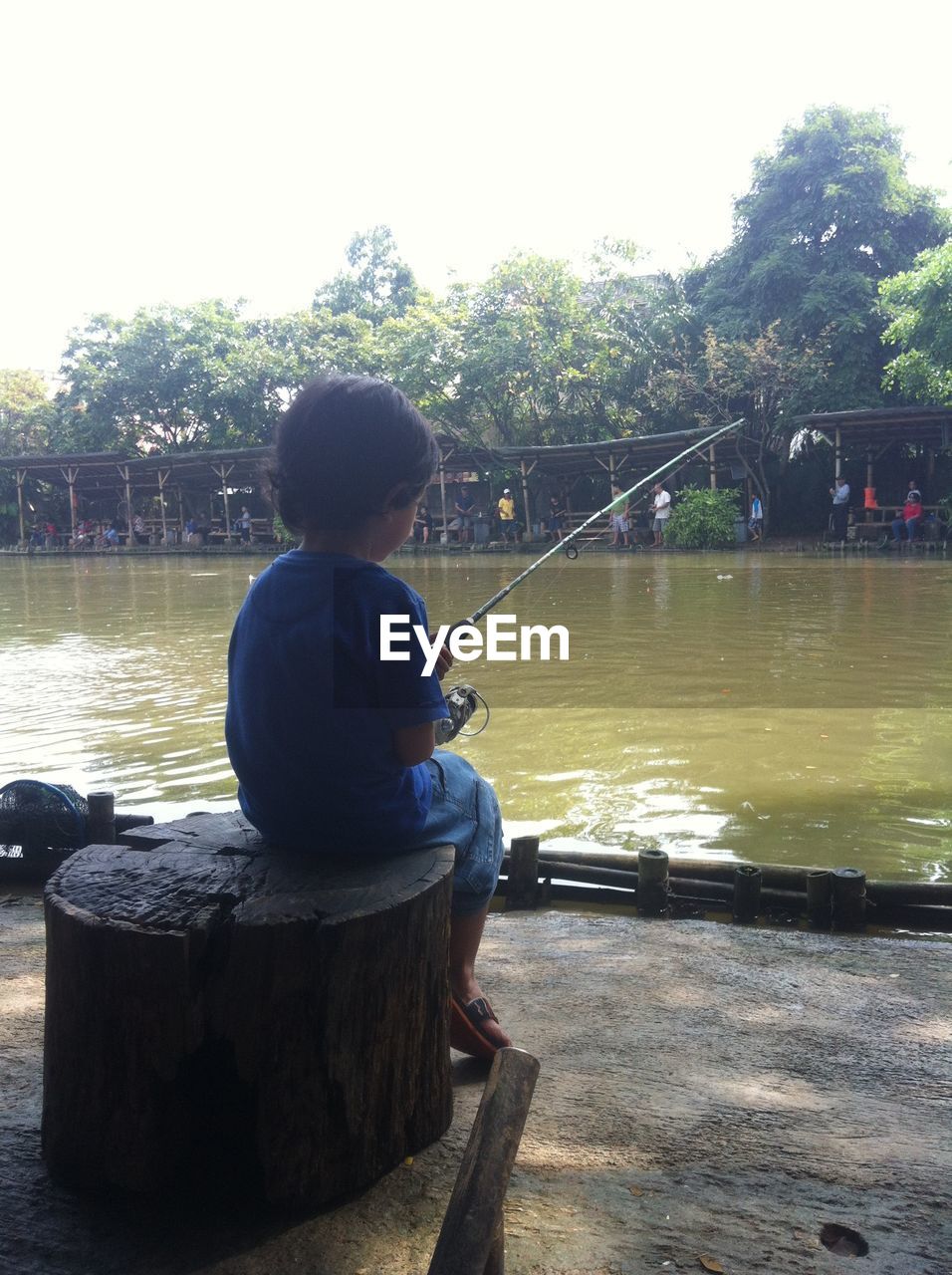 REAR VIEW OF GIRL SITTING ON RIVERBANK AGAINST SKY