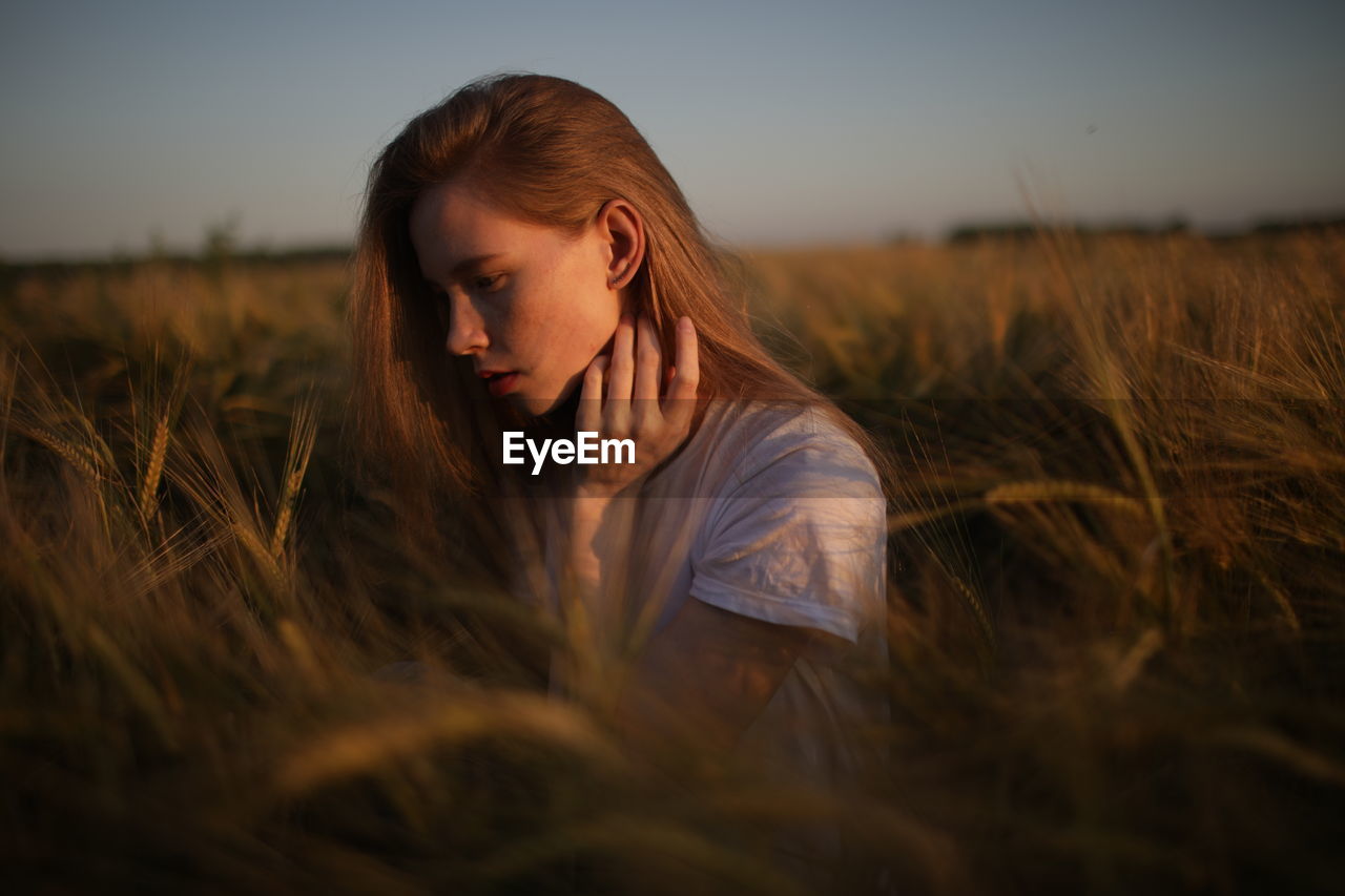 Young woman looking away on field against sky during sunset