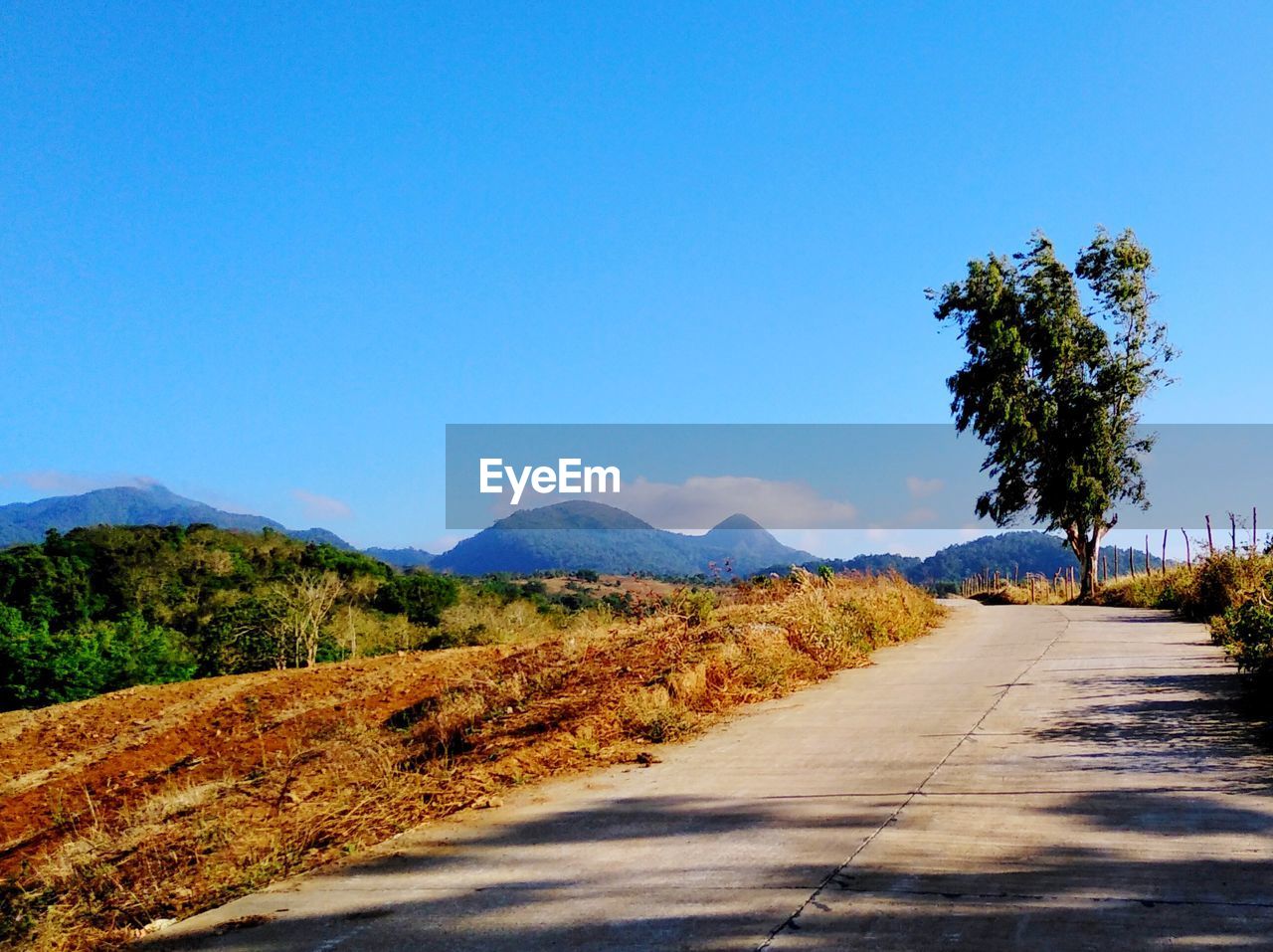 Scenic view of road by mountains against clear blue sky