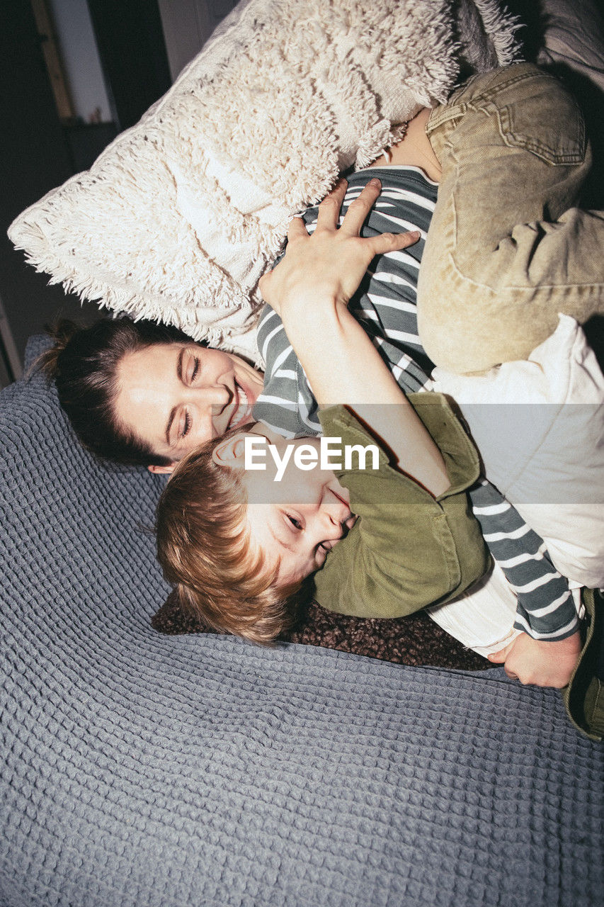 High angle view of happy woman embracing son while lying on bed at home