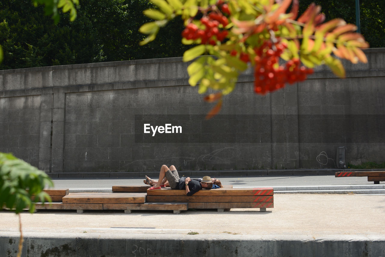 PEOPLE SITTING ON SIDEWALK AGAINST WALL