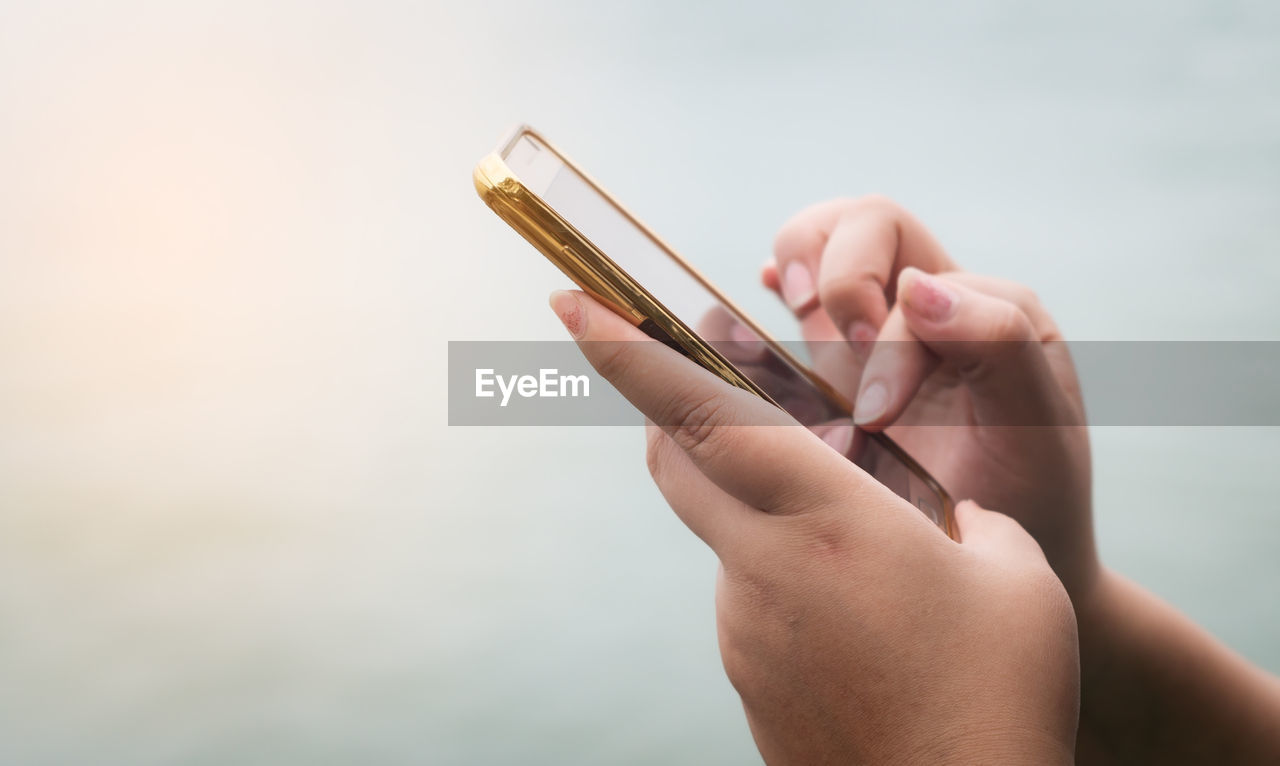 Cropped hands of woman using mobile phone against sky