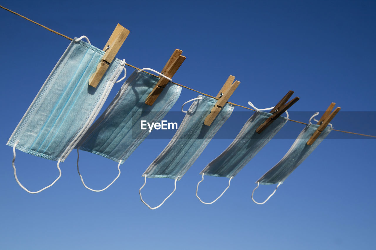 Low angle view of clothespins hanging on rope against blue sky