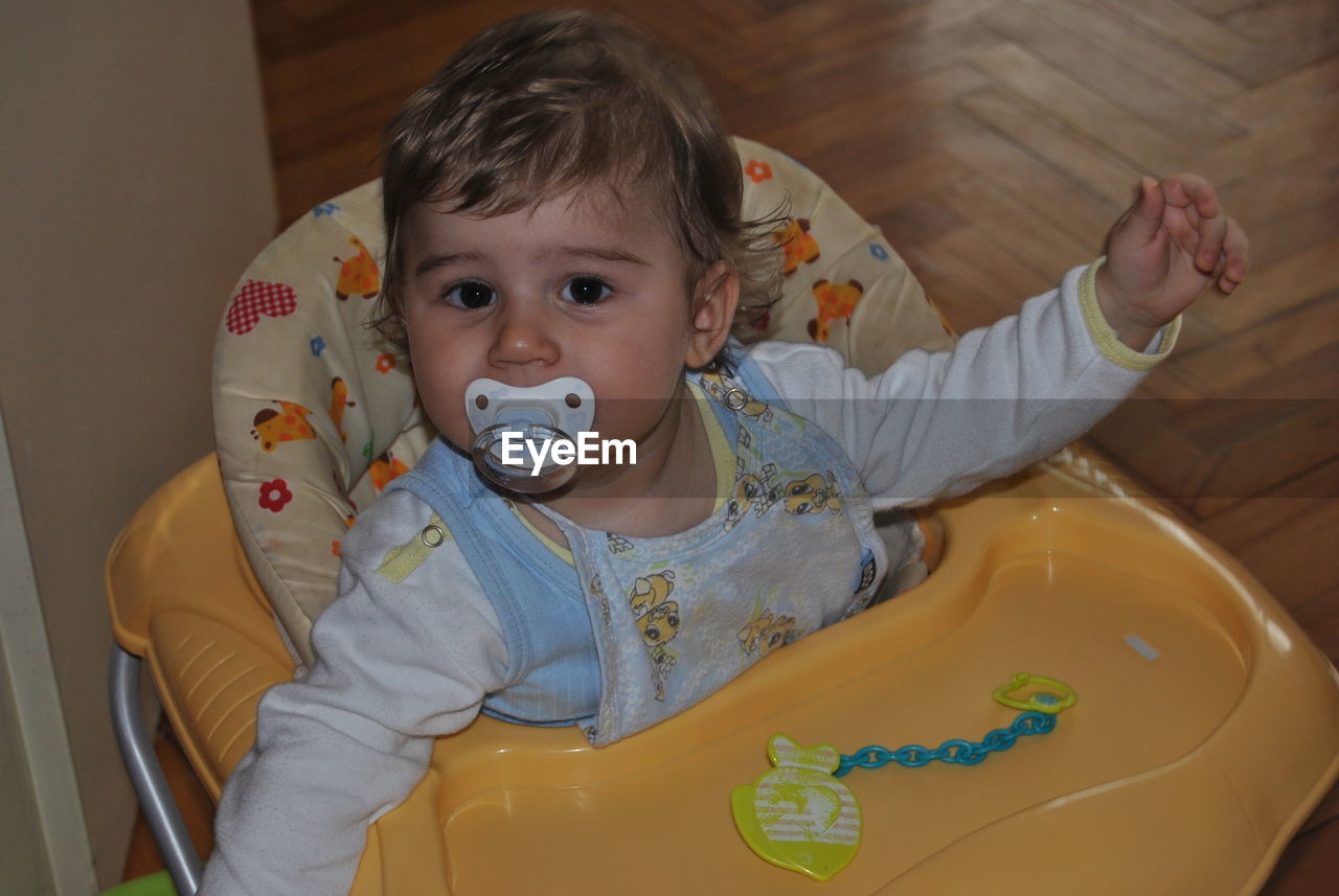 Portrait of cute baby boy sucking pacifier in walker at home