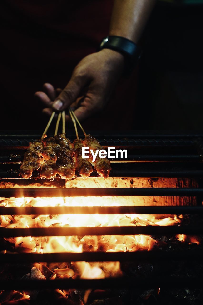 Cropped image of man cooking food on barbecue at night