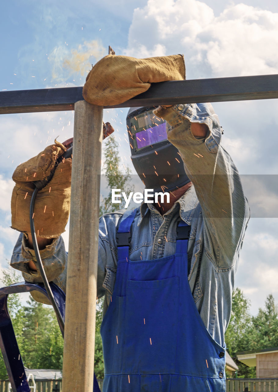 Man welder in a welding mask, construction uniform protective gloves cooks metal on  site.