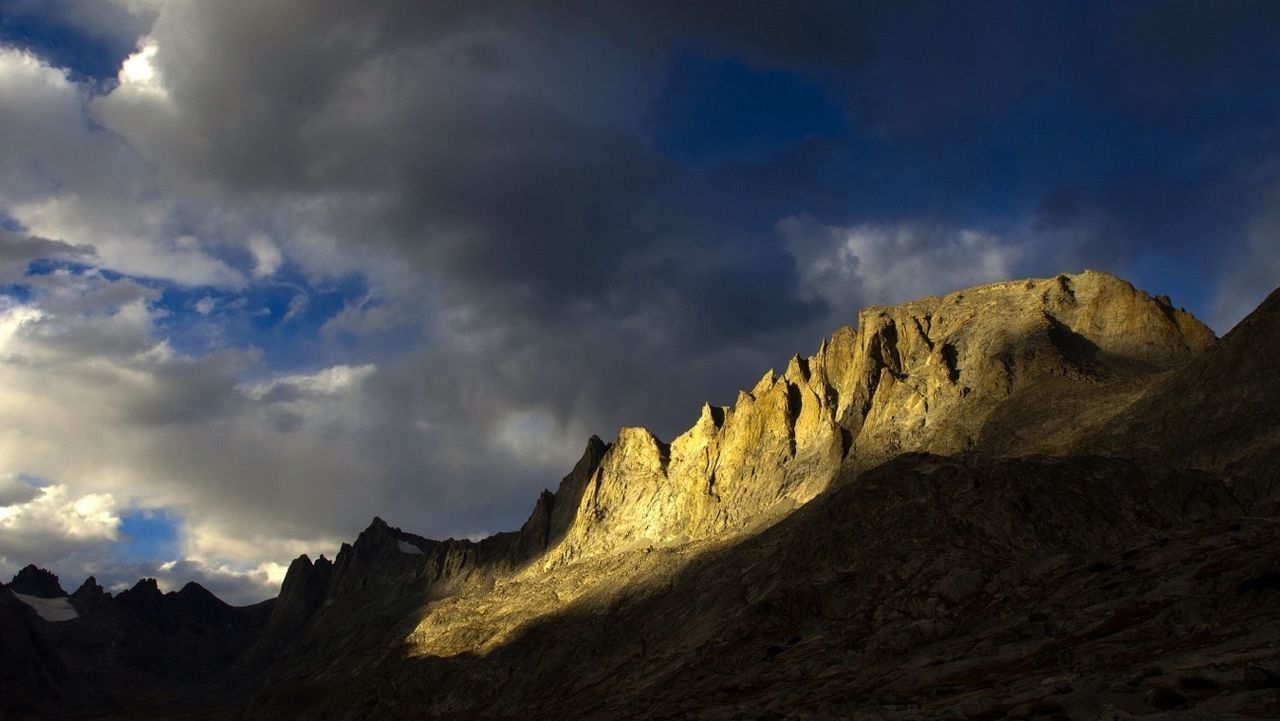 Low angle view of mountains against cloudy sky on sunny day