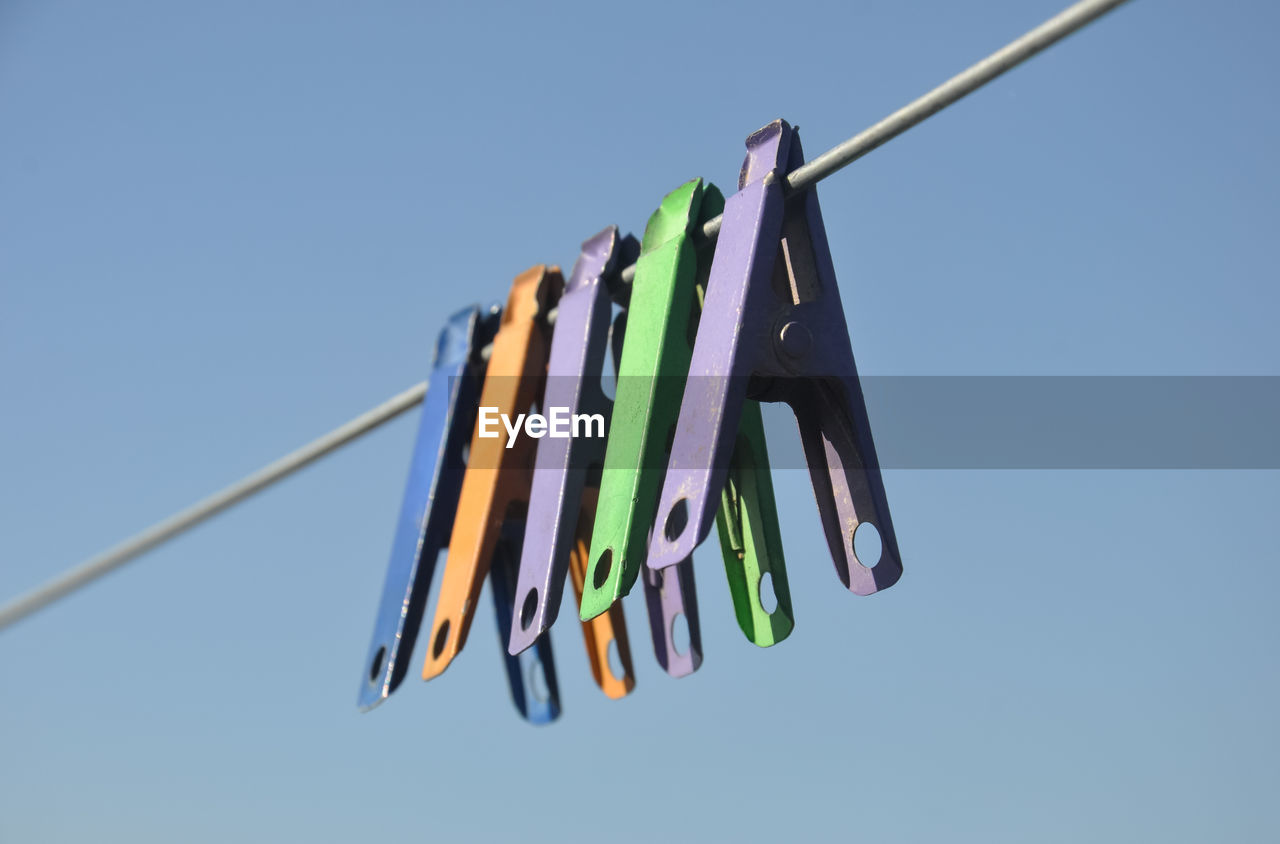 Low angle view of multi colored clothespins hanging against blue sky