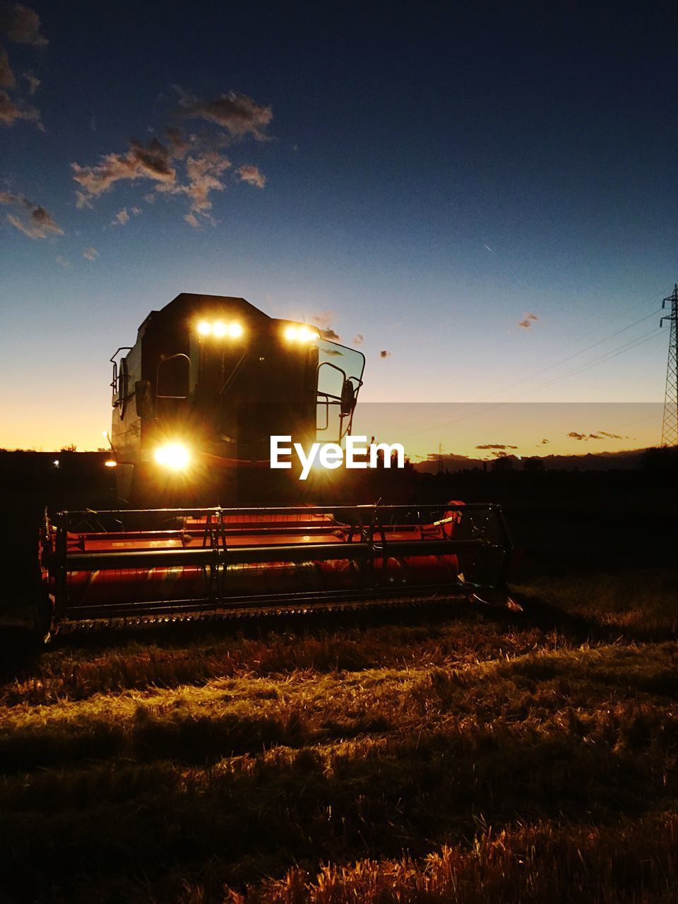 Combine harvester on field against sky during sunset