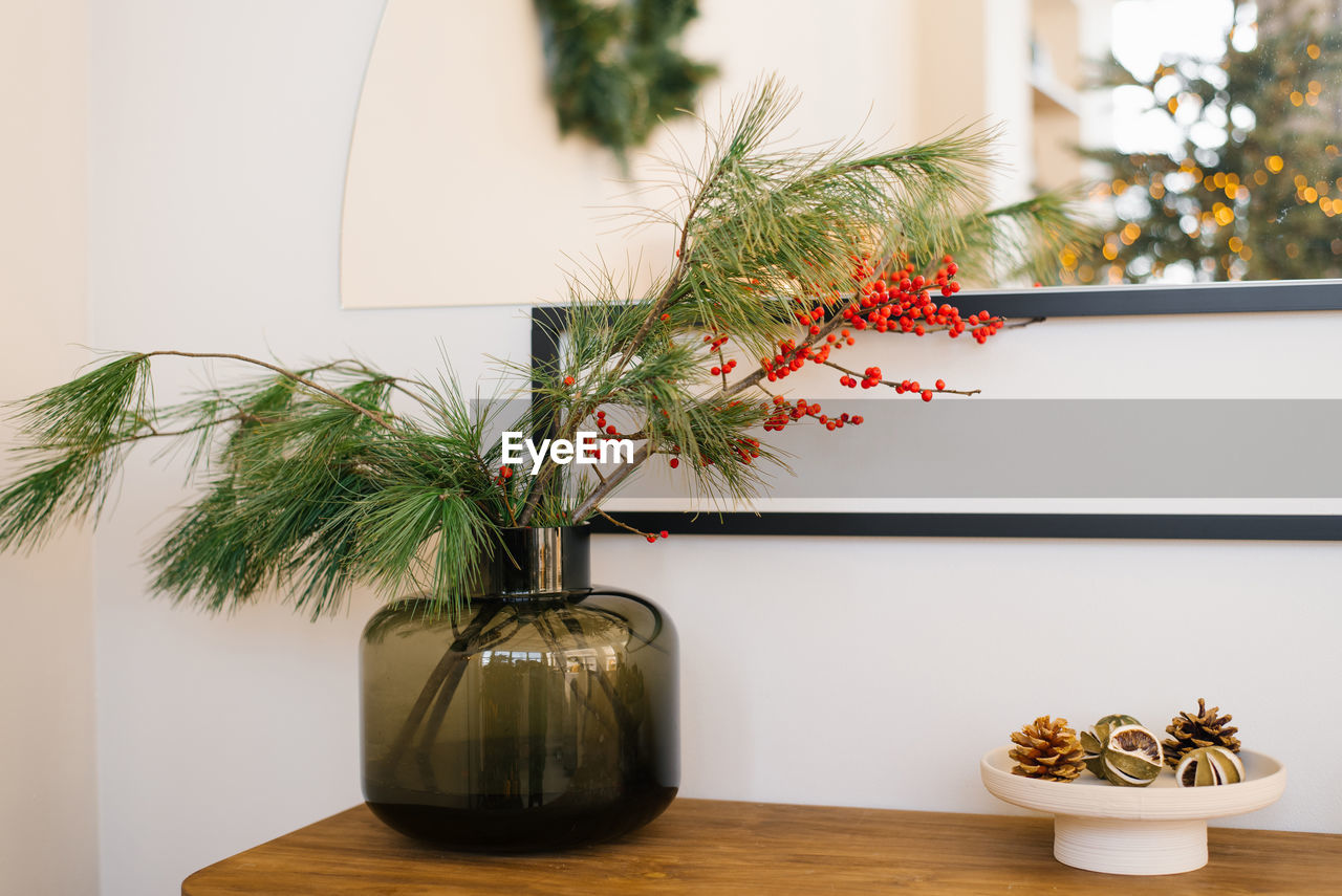 Pine branches and red berries in a glass jar vase. christmas decor in the interior of a cozy house