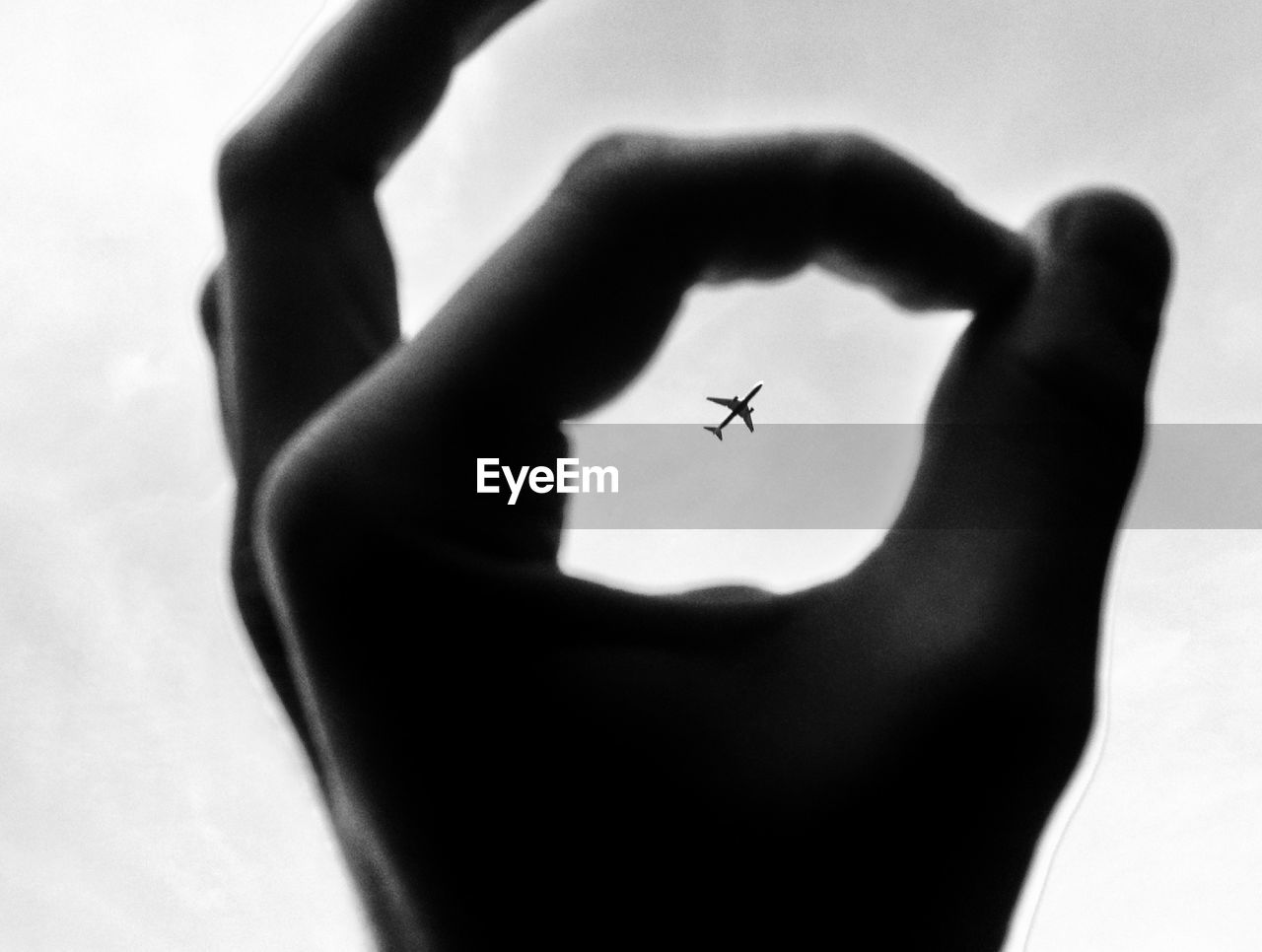 Low angle view of airplane in flight seen through fingers