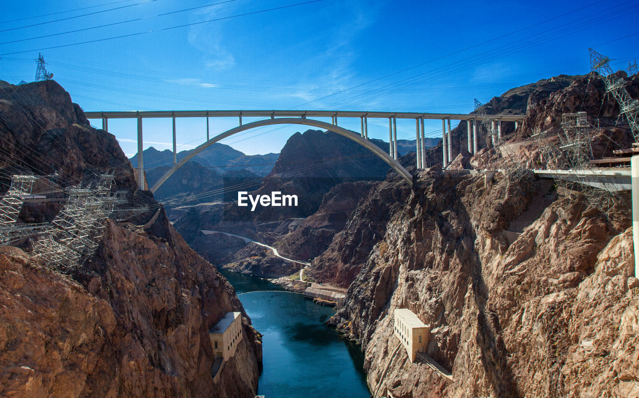 bridge, water, architecture, nature, built structure, sky, travel destinations, scenics - nature, transportation, travel, rock, environment, blue, river, no people, mountain, beauty in nature, tourism, arch, landscape, power generation, outdoors, coast, land, hydroelectric power, dam, day, city, canyon, rock formation, environmental conservation, electricity, mountain range, cloud, sunlight