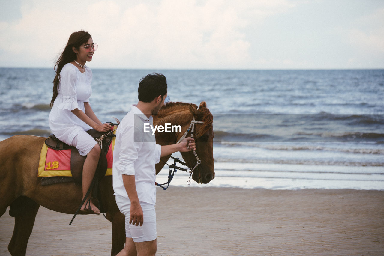 Young woman with boyfriend riding horse at beach