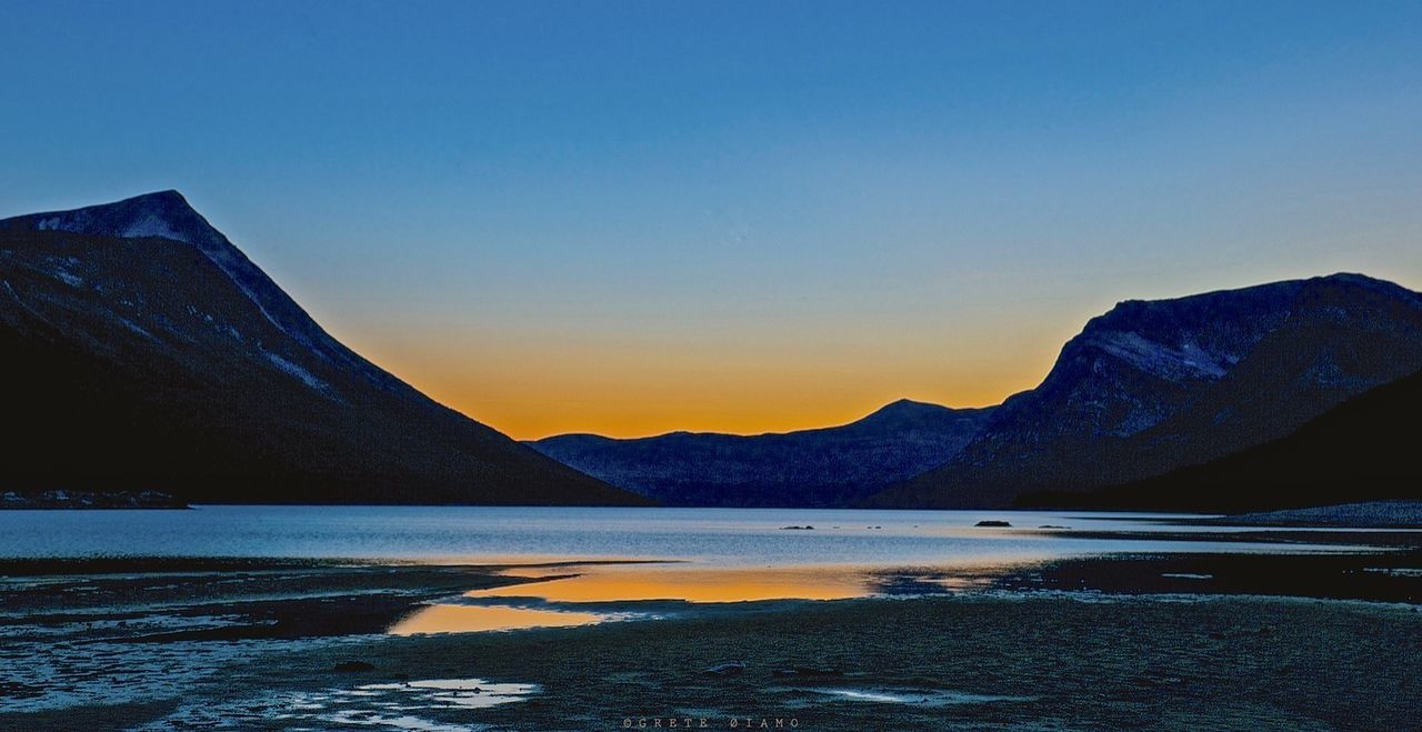 Scenic view of lake and mountains against clear sky at sunset