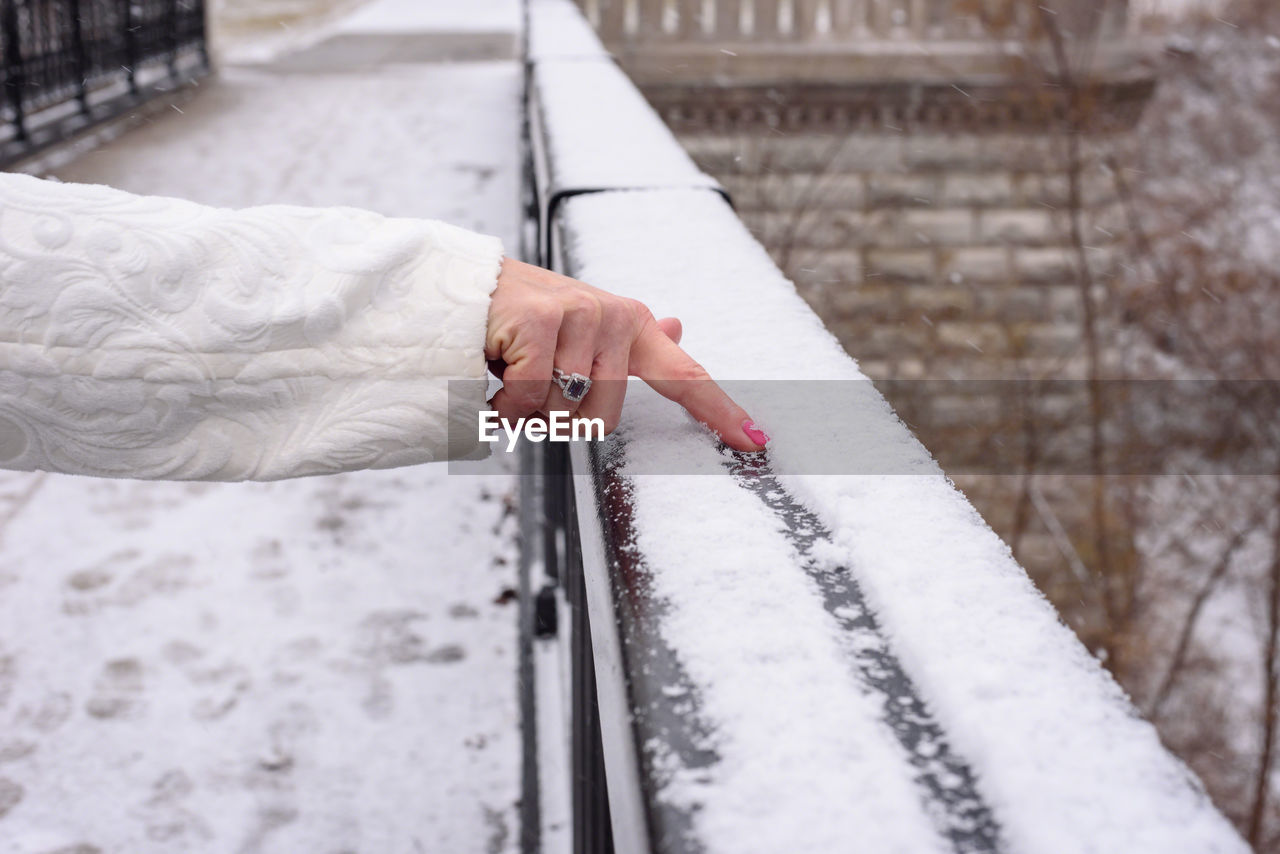 Cropped hand of woman making line in snow on railing