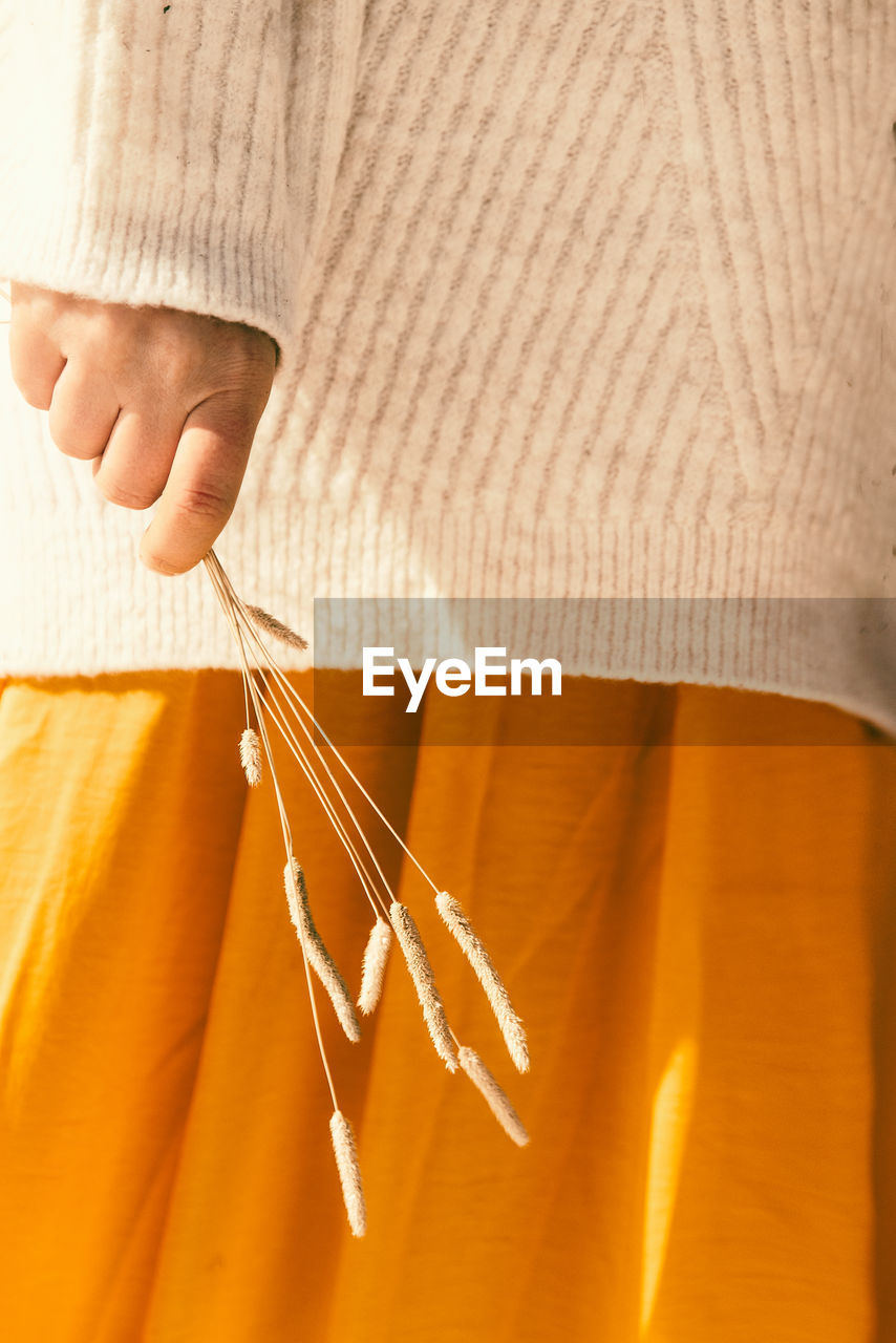 Woman in orange skirt holding dry spikelets in her hands
