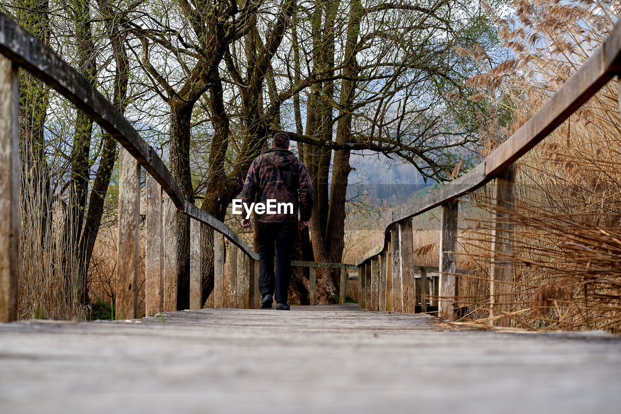 REAR VIEW OF MAN WALKING ON FOOTPATH