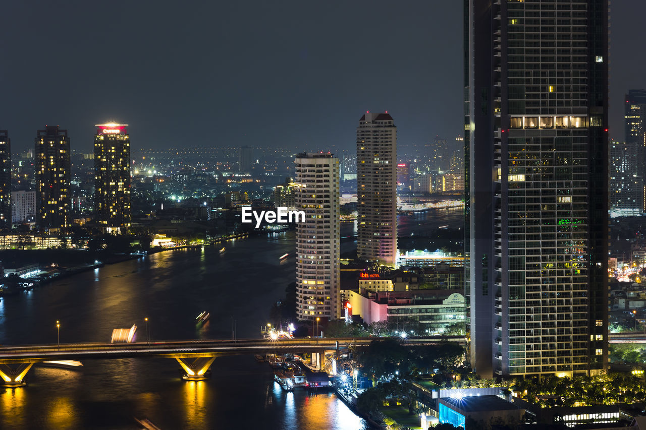 Illuminated buildings by river against sky at night