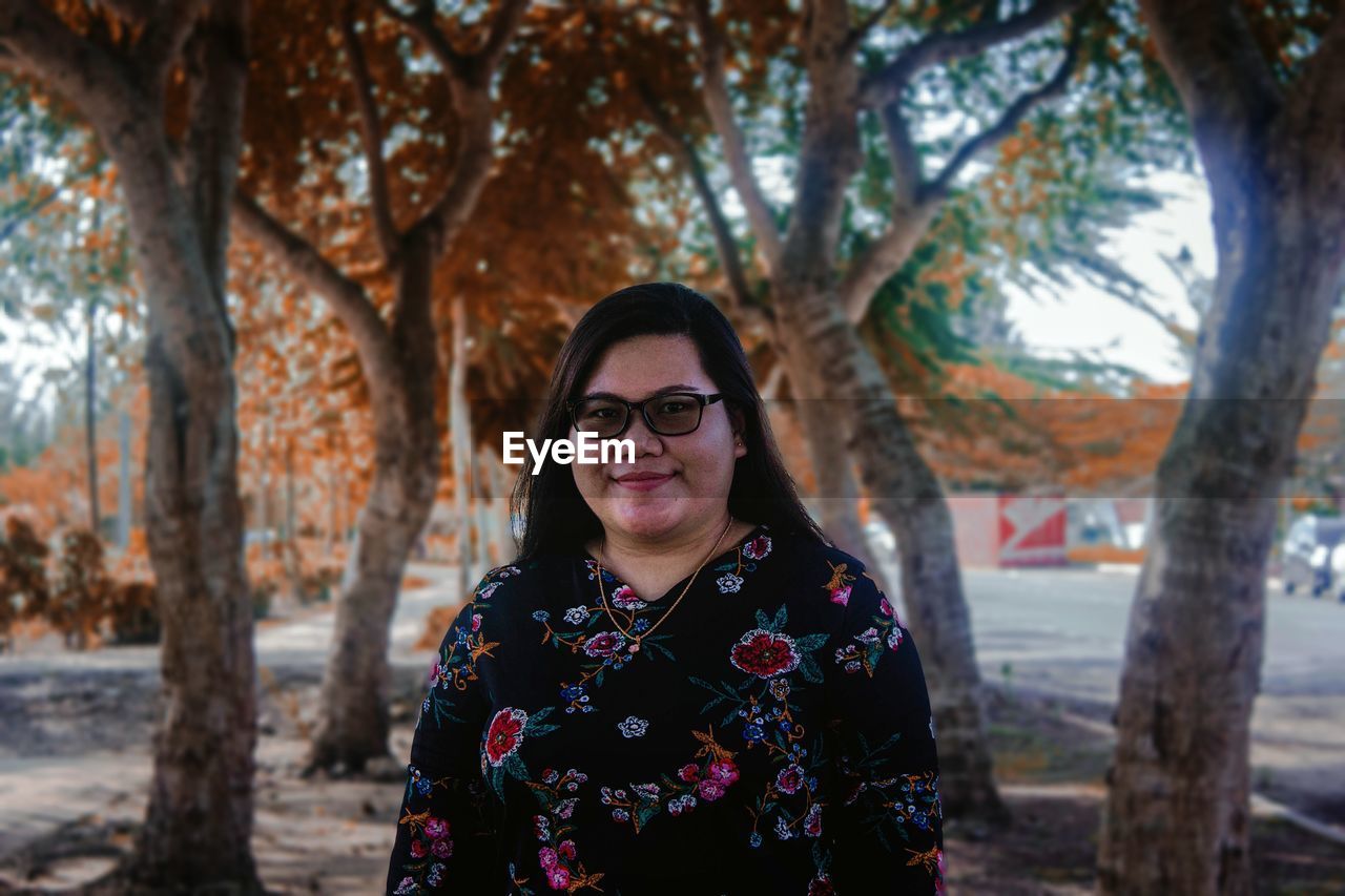 Portrait of smiling young woman standing by tree