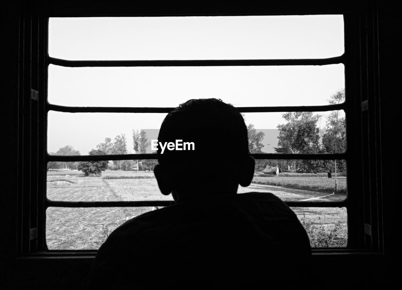 REAR VIEW OF MAN LOOKING THROUGH GLASS WINDOW