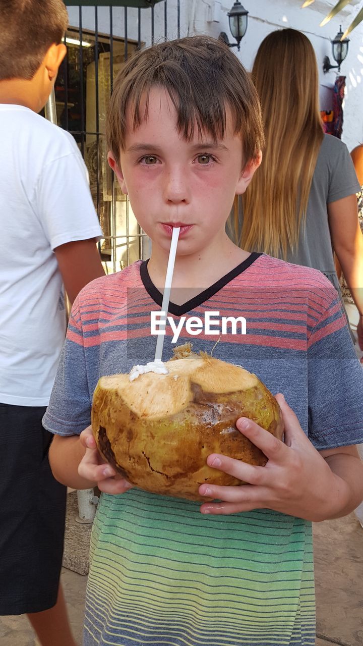 Portrait of boy having coconut while standing outdoors