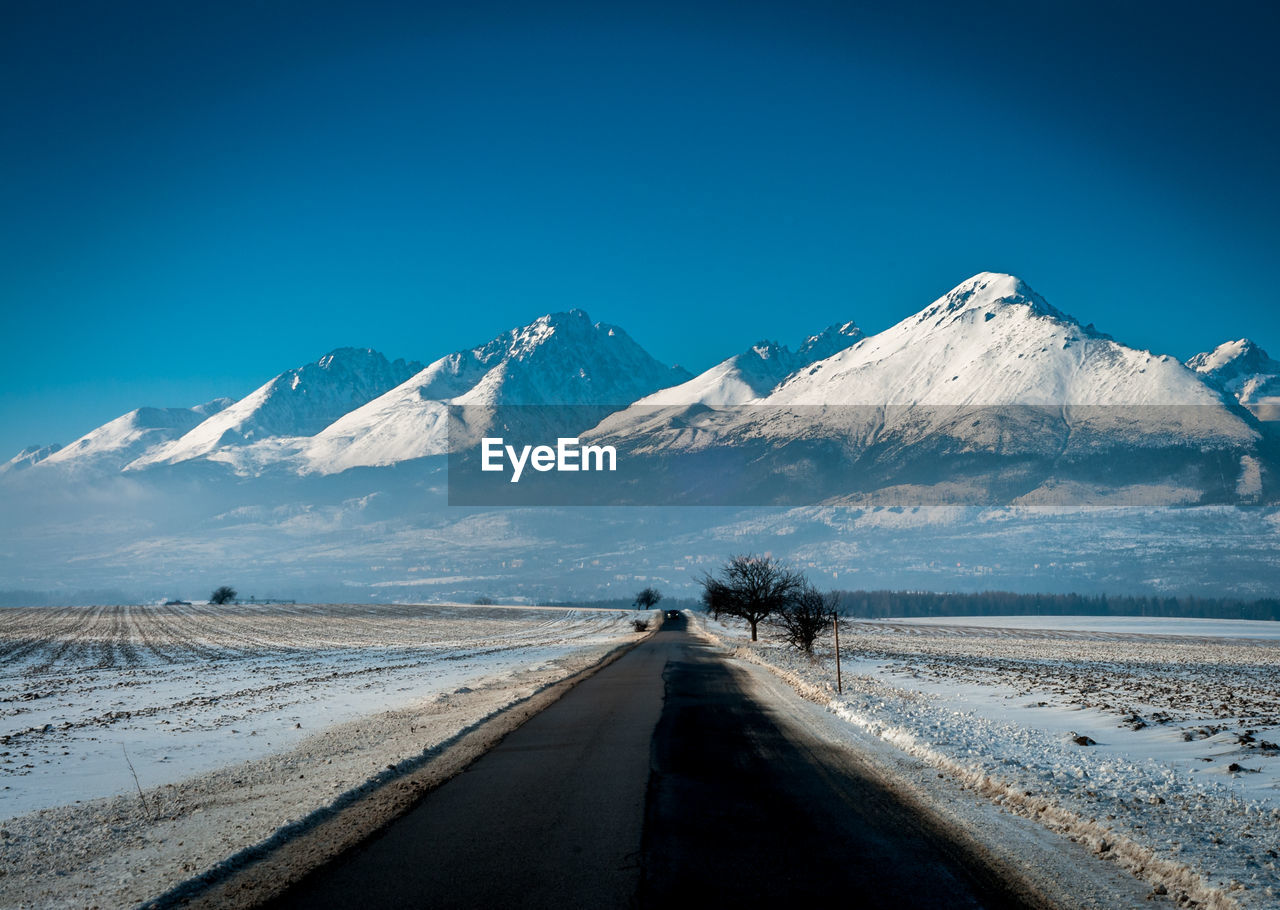 Road by snowcapped mountains against clear blue sky