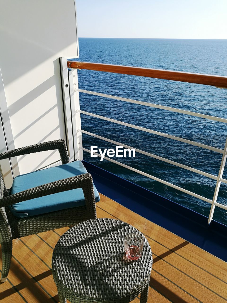 Empty chair and table on ship balcony by sea against clear sky