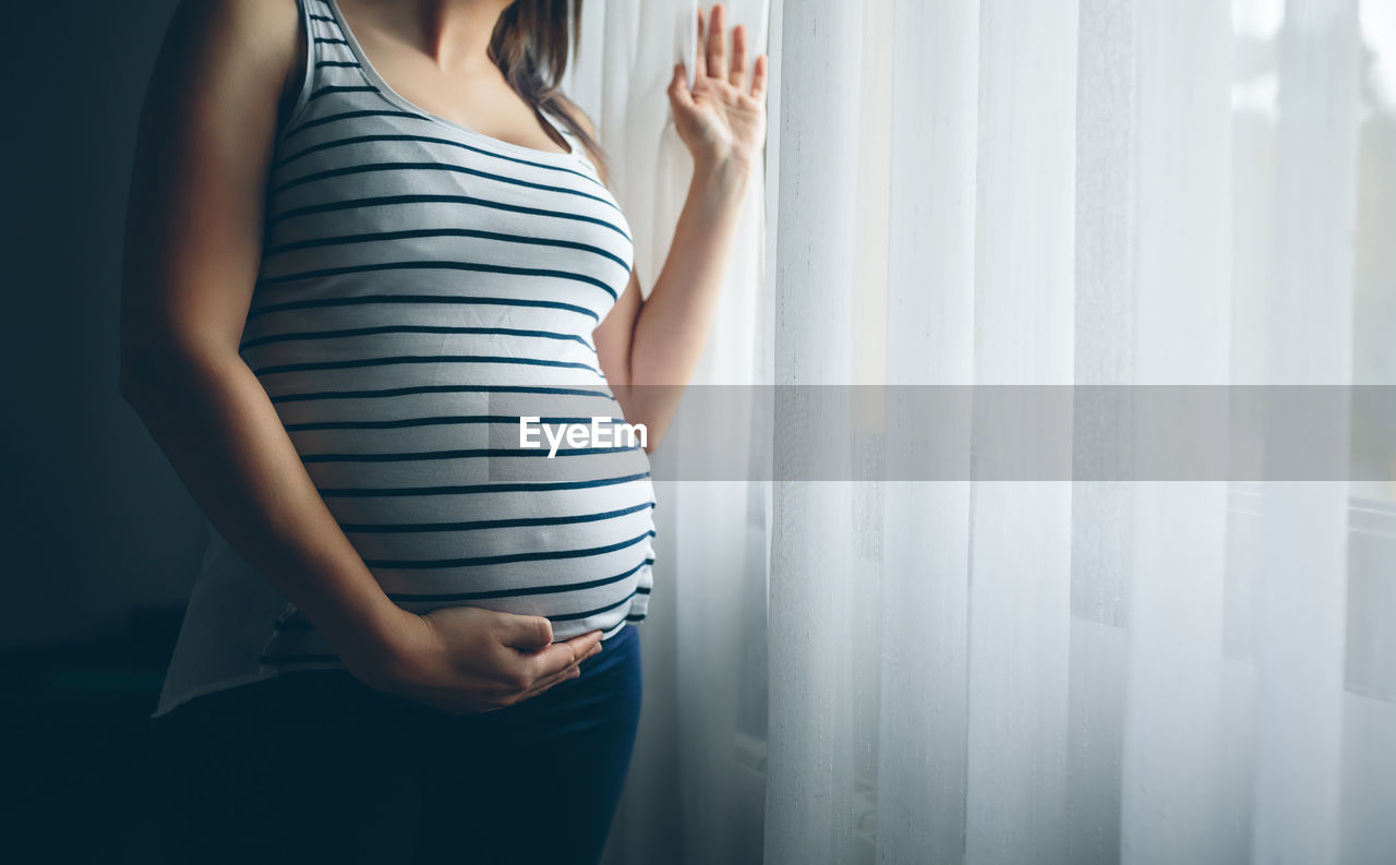 Midsection of pregnant woman standing at home