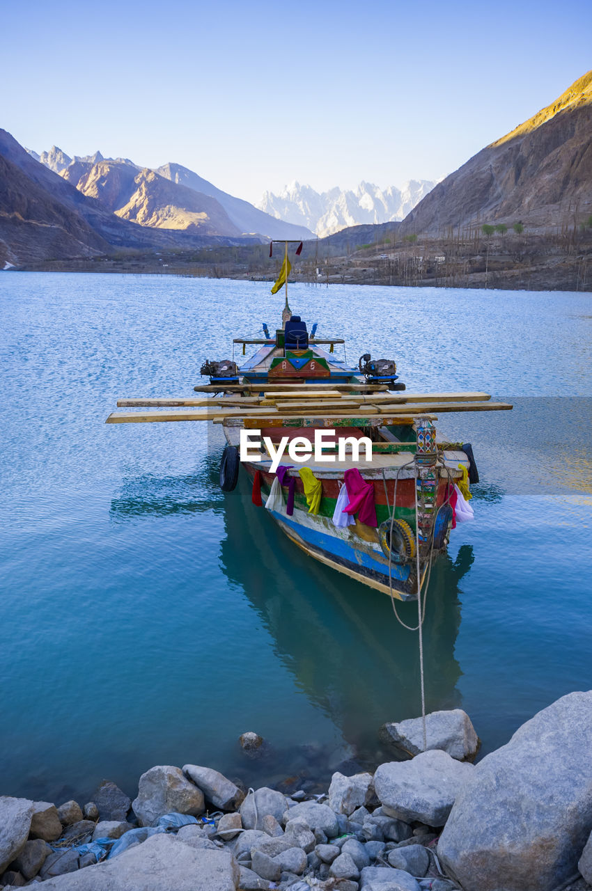 Boat moored on lake by mountains against clear sky