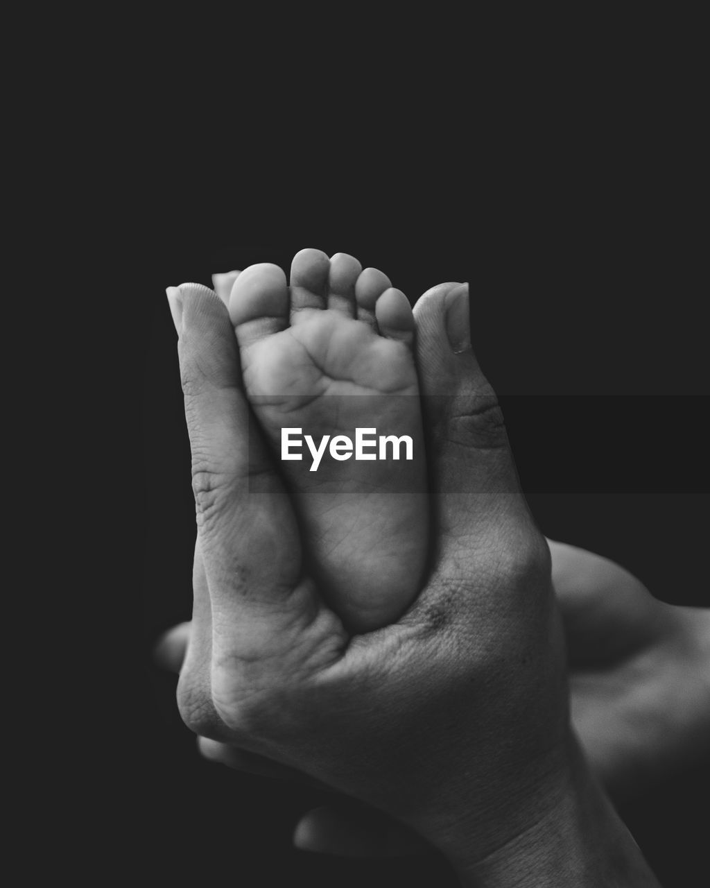 Close-up of human hand and baby foot against black background