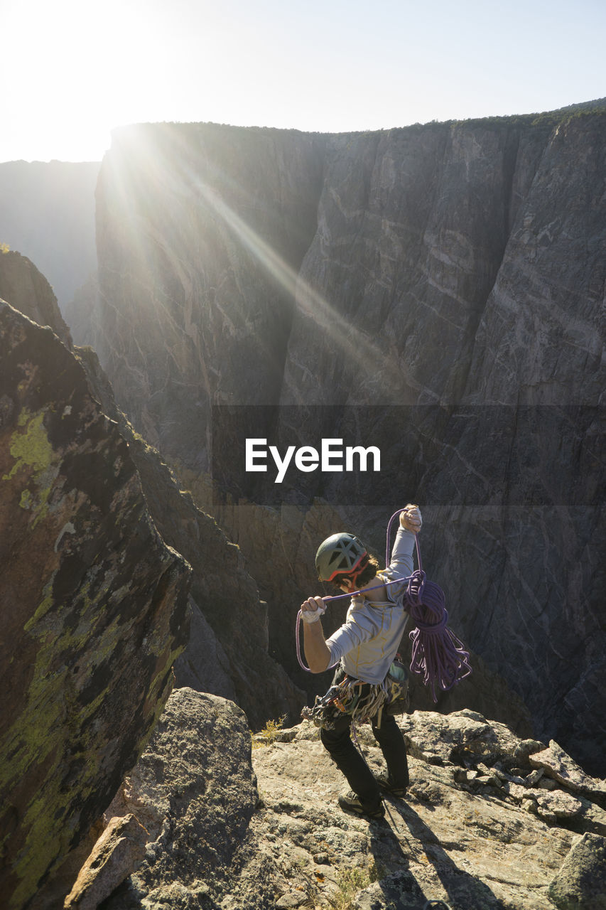 High angle view of man with rope standing on mountain against sky during sunny day