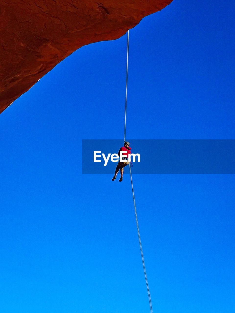 Low angle view of person climbing on rope against clear blue sky