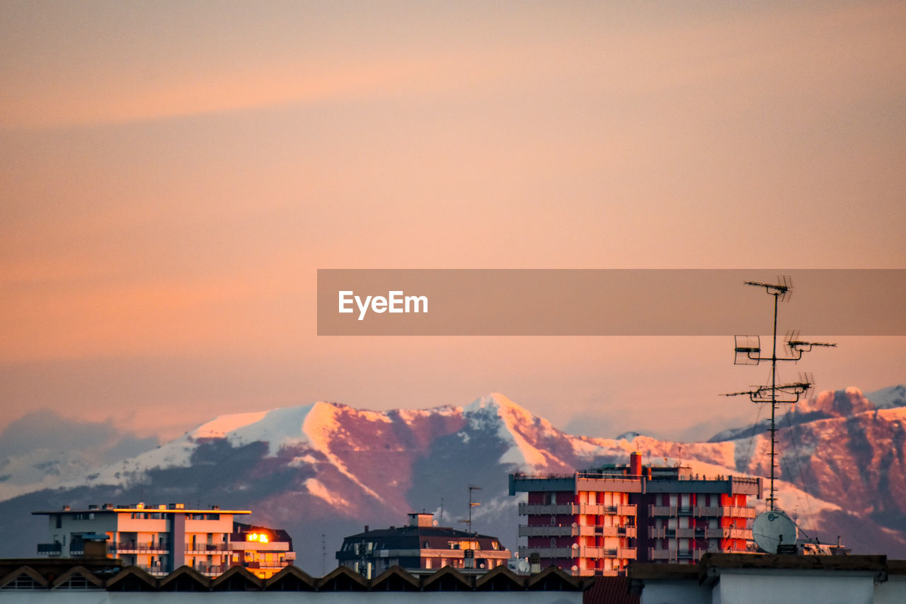 Buildings and mountains against sky at sunset