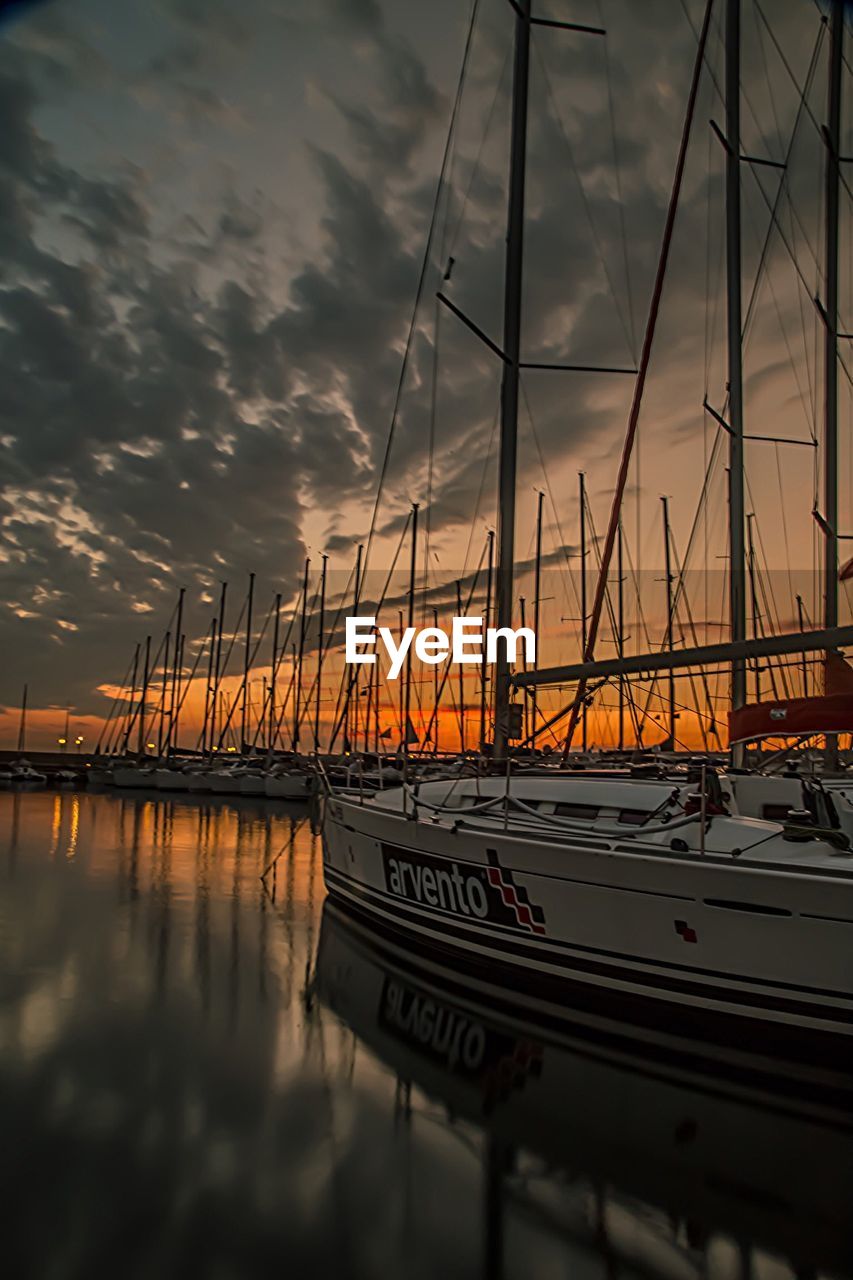 Sailboats moored at harbor in sea against sky during sunset