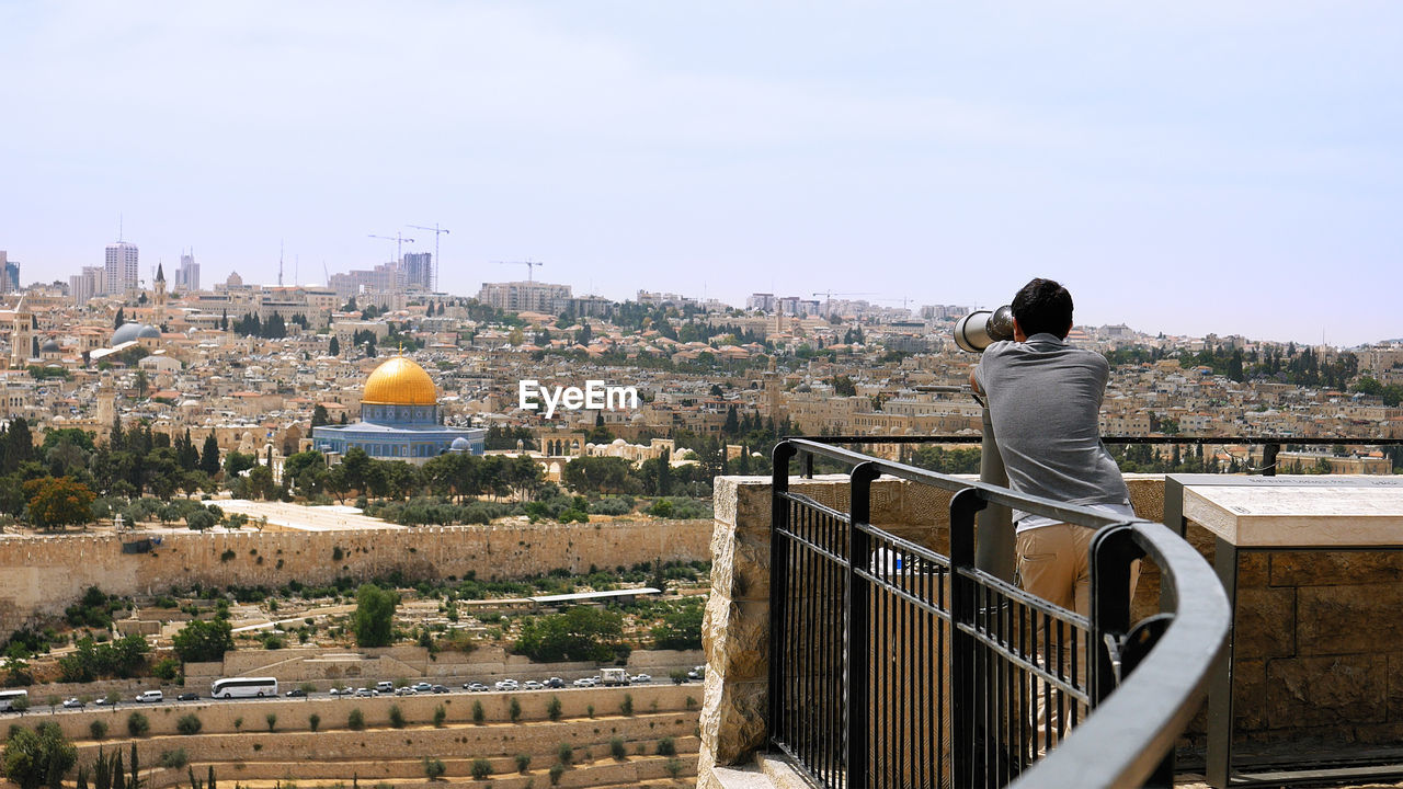 Rear view of man looking at cityscape during sunny day