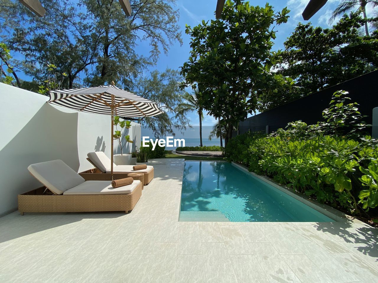 swimming pool, luxury, wealth, water, nature, tree, villa, architecture, estate, plant, sunlight, poolside, backyard, tranquility, built structure, chair, no people, relaxation, furniture, patio, lounge chair, house, day, outdoors, building, summer, building exterior, lifestyles, sky, home, tourist resort, travel destinations, deck, tranquil scene, residential district, vacation, trip, holiday, front or back yard, idyllic, home ownership, seat, beauty in nature, table, tropical climate, sunny, holiday villa, luxury hotel, blue, mansion, real estate, domestic life, scenics - nature