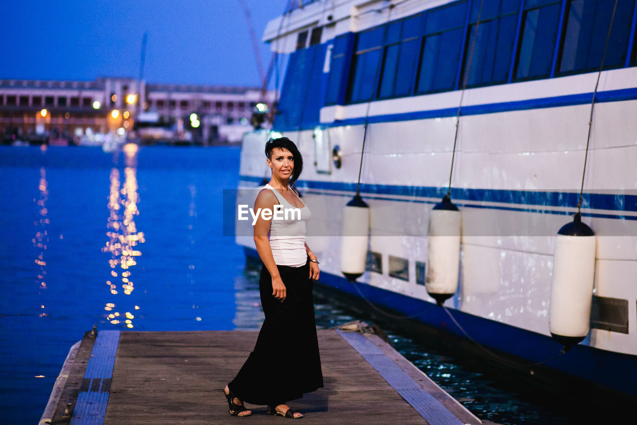 Full length portrait of young woman standing at harbor