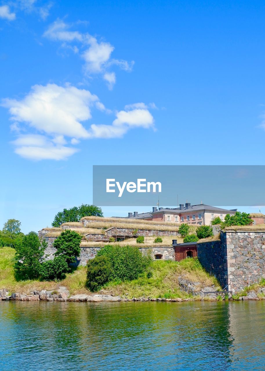 Buildings by river against blue sky