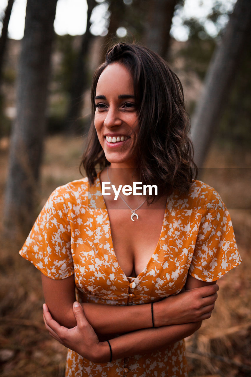 Close-up of smiling young woman looking away standing in forest