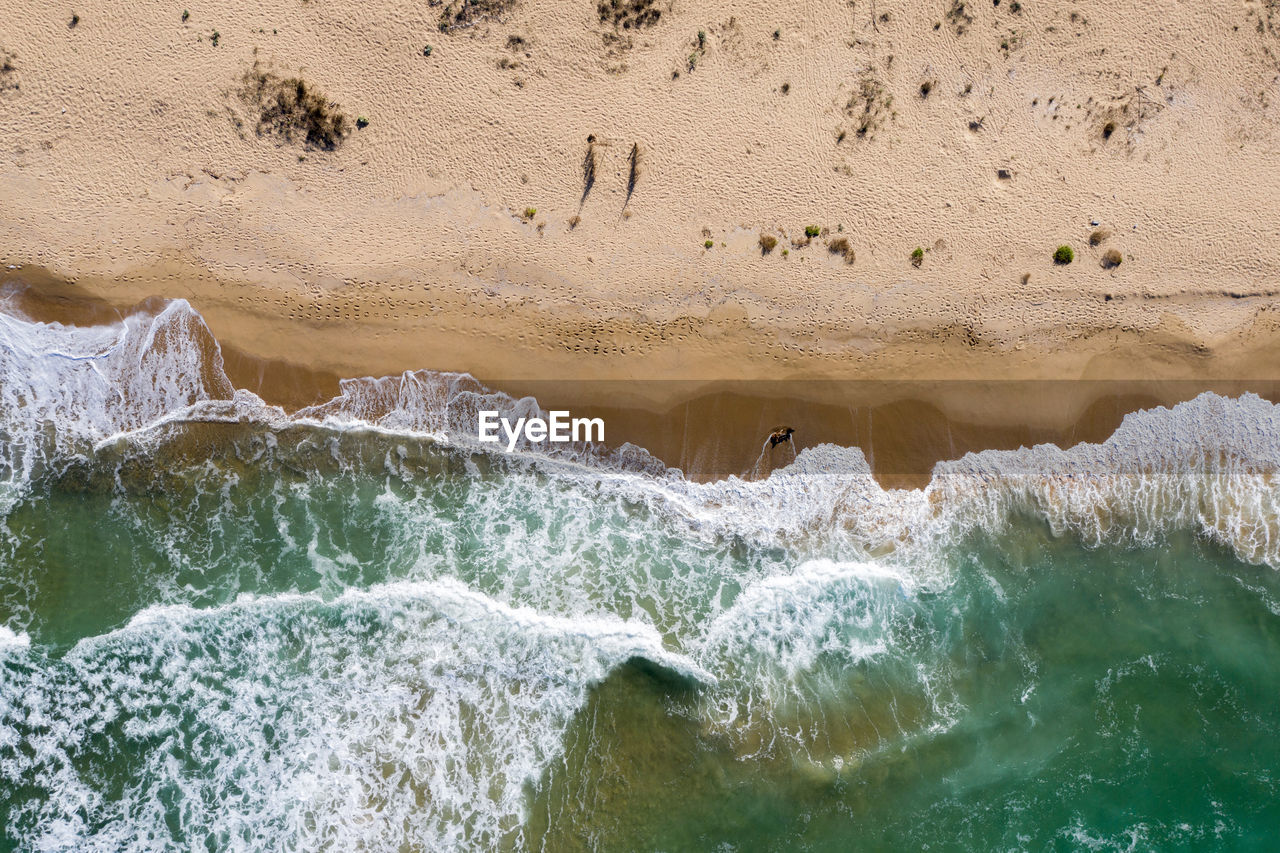 Aerial view of ocean waves washing a secluded sandy shoreline beach