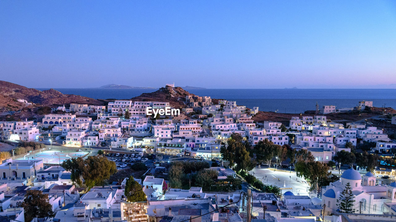 High angle view of townscape by sea against clear blue sky