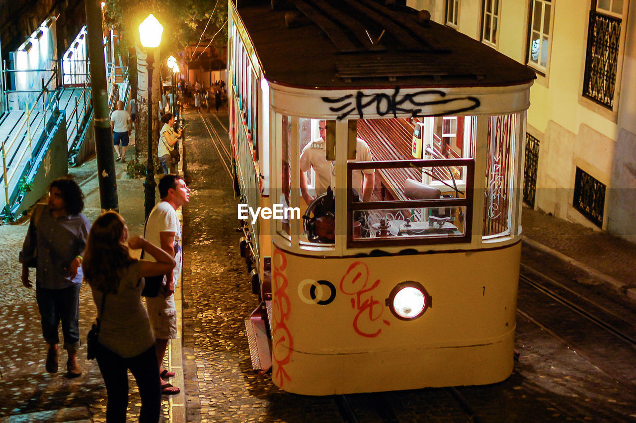 People on sidewalk by train tramp at night