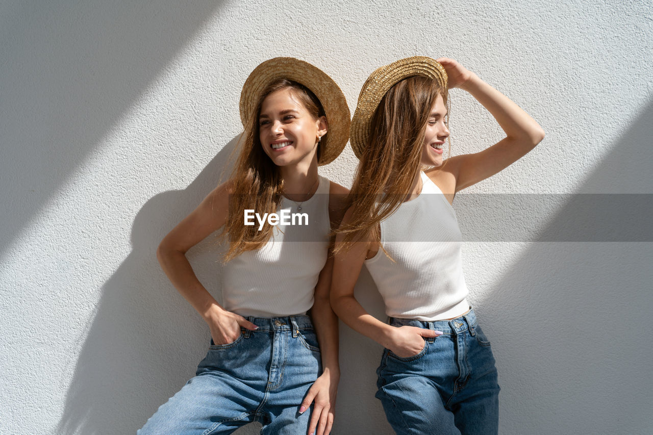 Young women wearing hat standing against wall