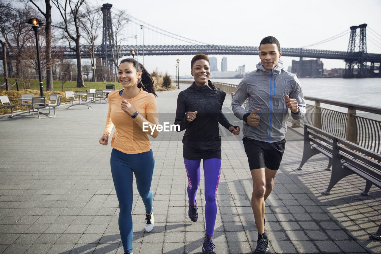 Happy multi-ethnic athletes running on footpath with williamsburg bridge in background