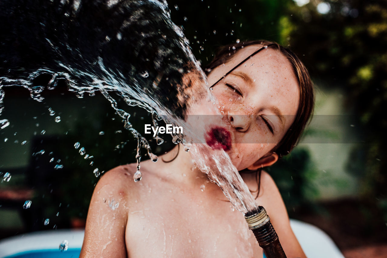 Young child drinking from a splashing hose outside in summer