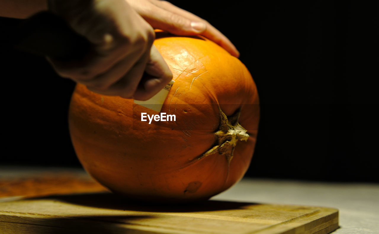 Cropped image of person carving pumpkin at table
