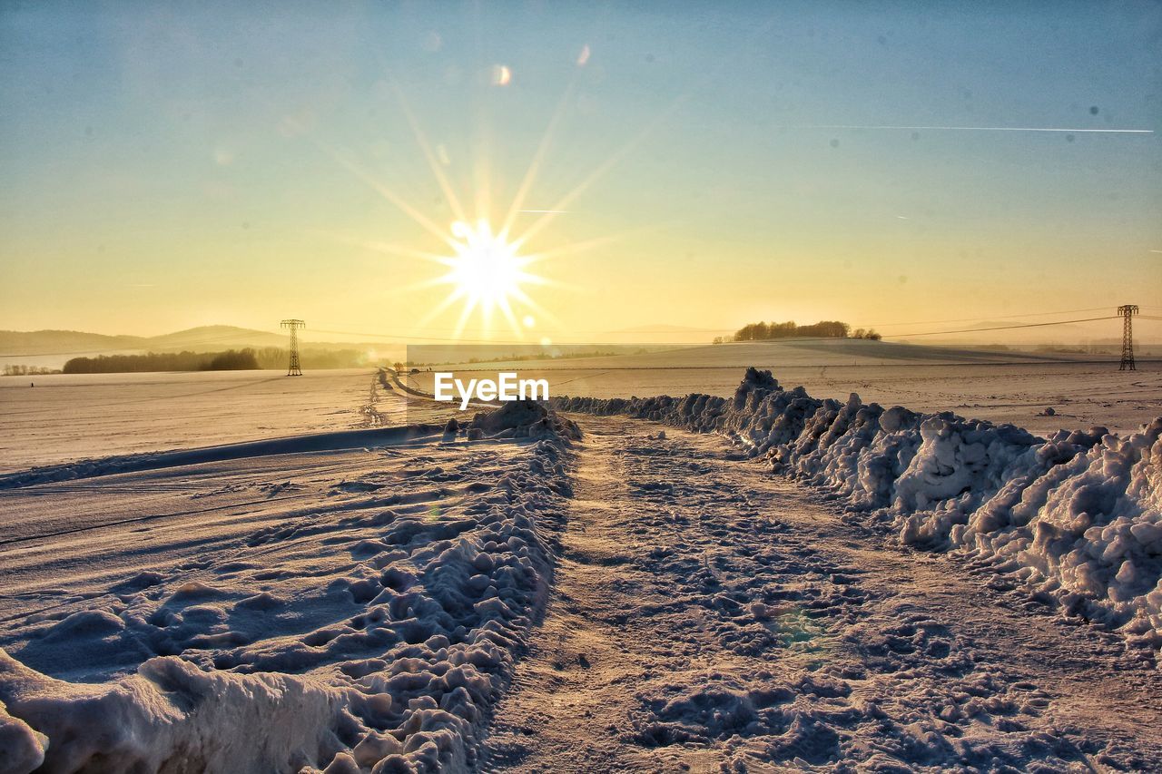 Snow covered landscape against sky during sunset
