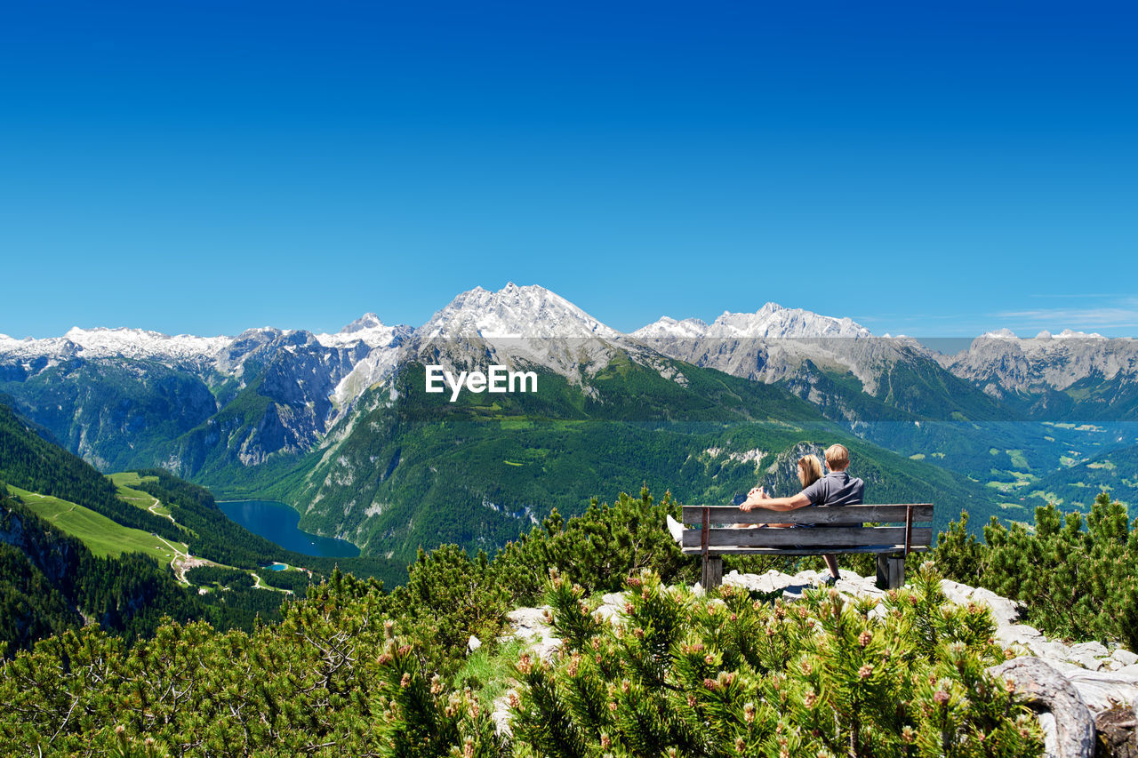 Couple sitting on a bench in front of the alps enjoying the mountain panorama